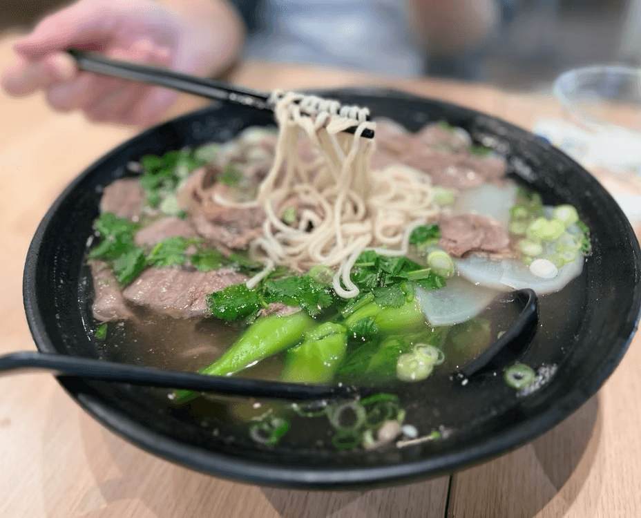 Hand-pulled noodles lifted with chopsticks from a bowl of beef noodle soup at 300G Noodles